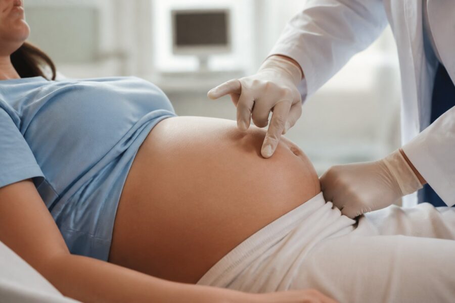 Profissional de saúde examinando a barriga de uma mulher grávida em consultório médico.