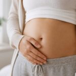 Mulher com um mês de gravidez tocando suavemente a barriga em um ambiente tranquilo.